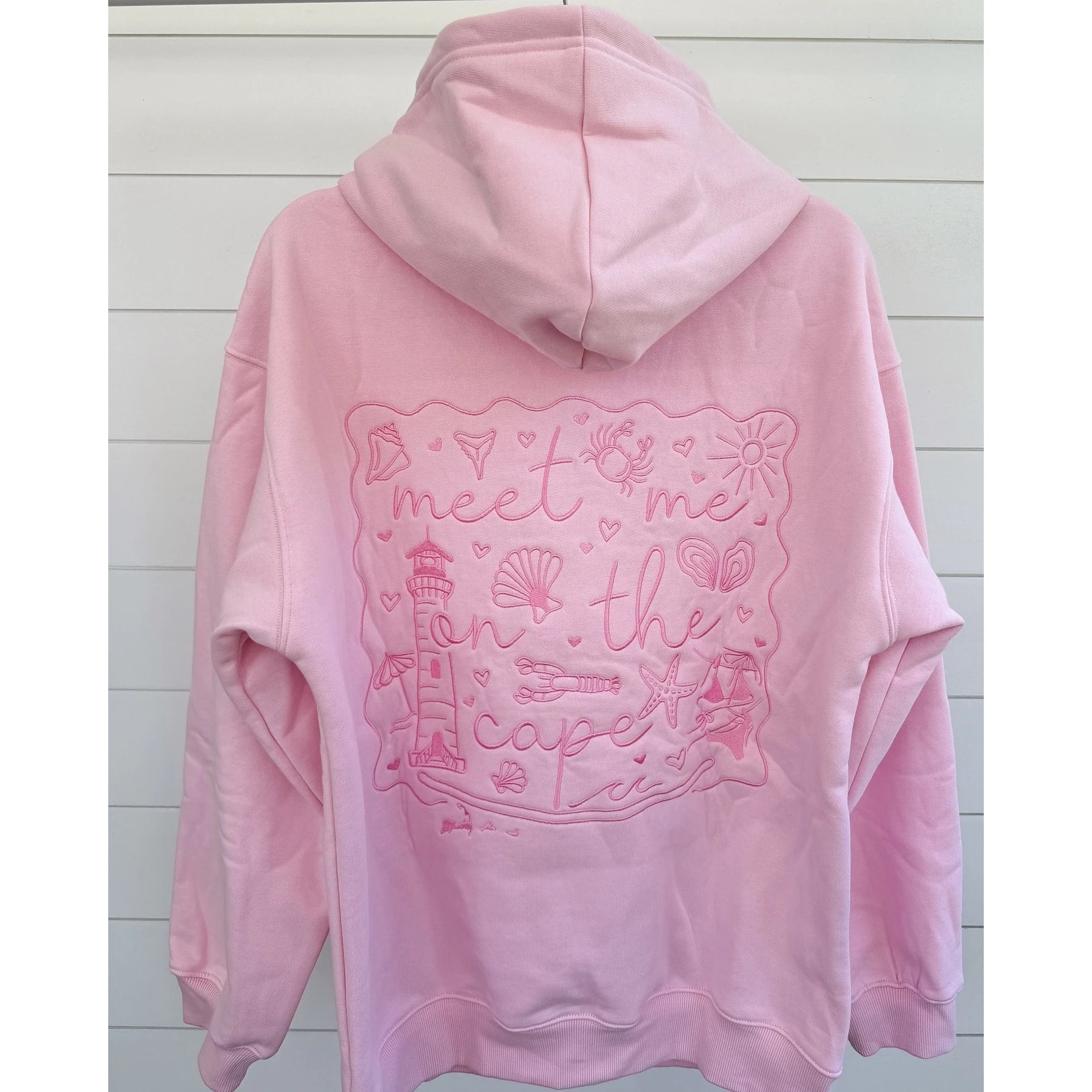 Pink hoodie with a decorative text design on the back against a light wooden panel background