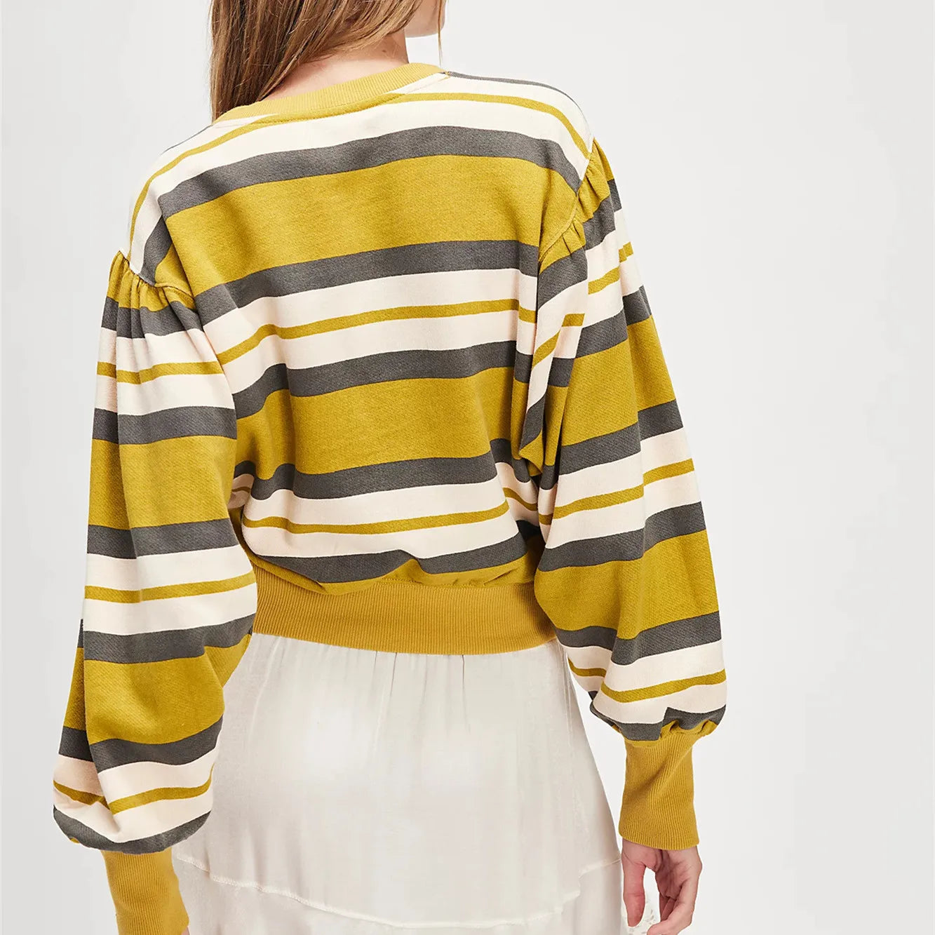 Person wearing a yellow, gray, and white striped sweater on a plain background