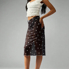 Woman wearing a white top and black polka dot skirt on a gray background