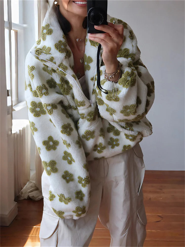 Person wearing a white sweater with green floral patterns in a room with wooden flooring.