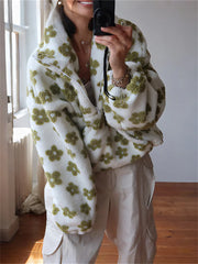 Person wearing a white sweater with green floral patterns in a room with wooden flooring.
