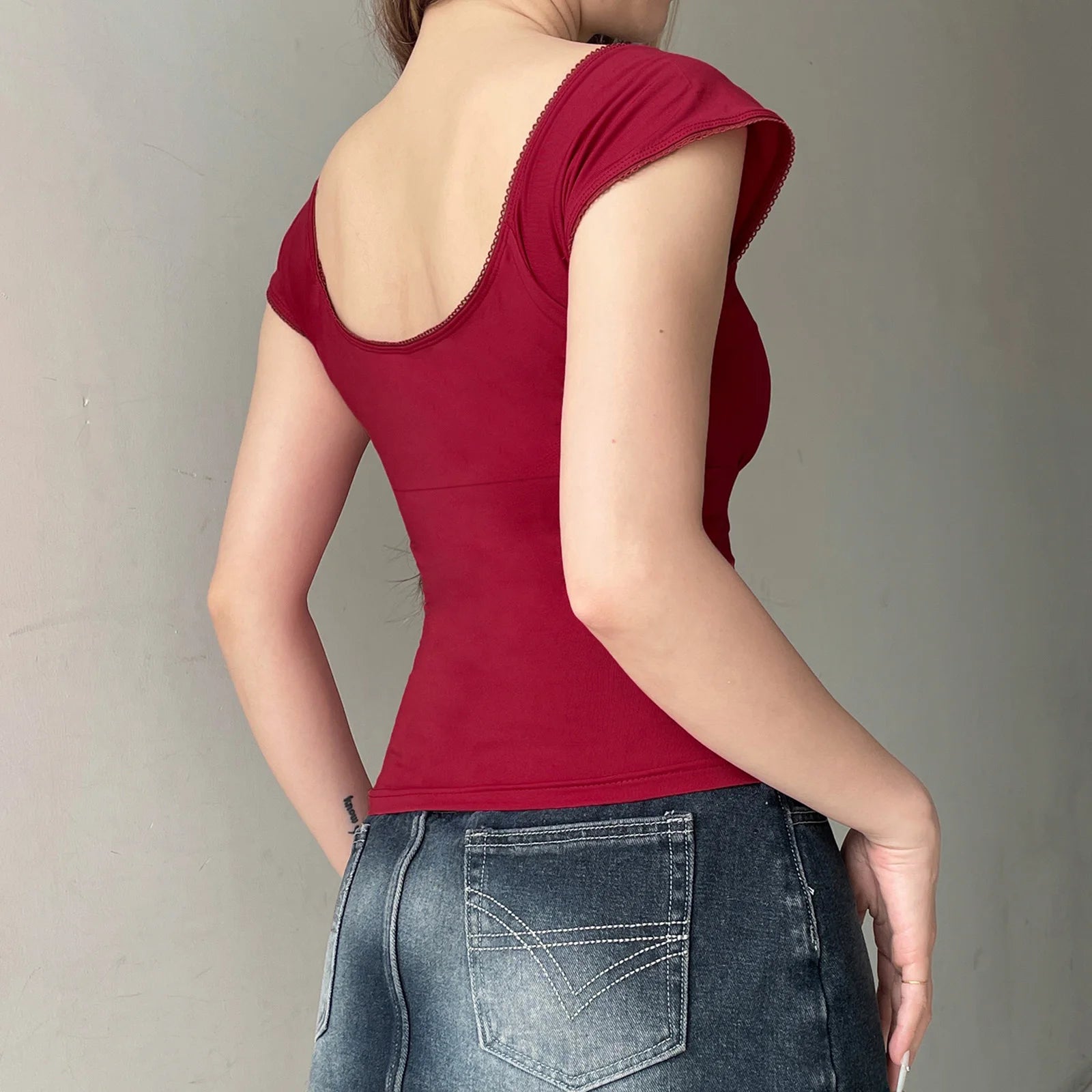 Person wearing a red sleeveless top and blue jeans against a neutral background
