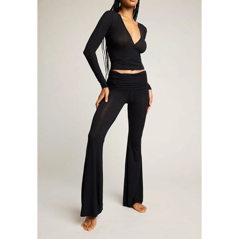 Person wearing a black outfit with a long-sleeve top and flared pants on a light gray background