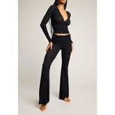 Person wearing a black outfit with a long-sleeve top and flared pants on a light gray background