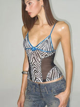 Woman wearing a zebra print top with blue straps and jeans against a plain background