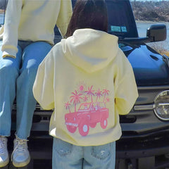 Person wearing a yellow hoodie with a pink graphic design sitting on a vehicle.