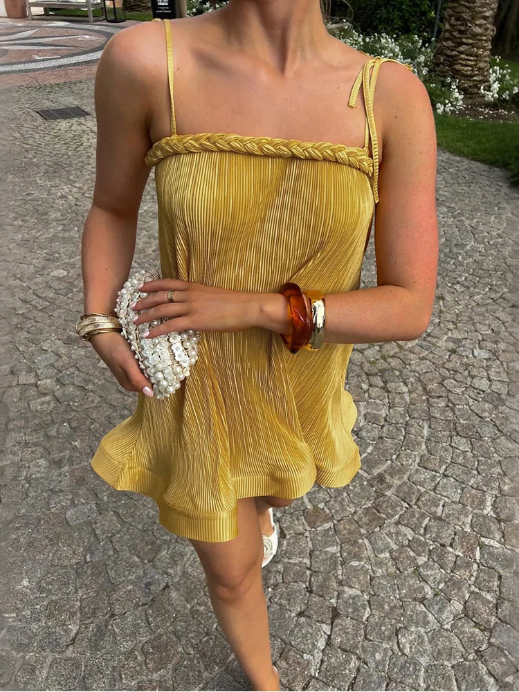 Person wearing a yellow dress with braided straps on a stone pavement.