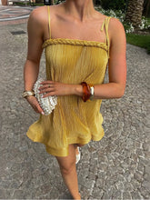 Person wearing a yellow dress with braided straps on a stone pavement.
