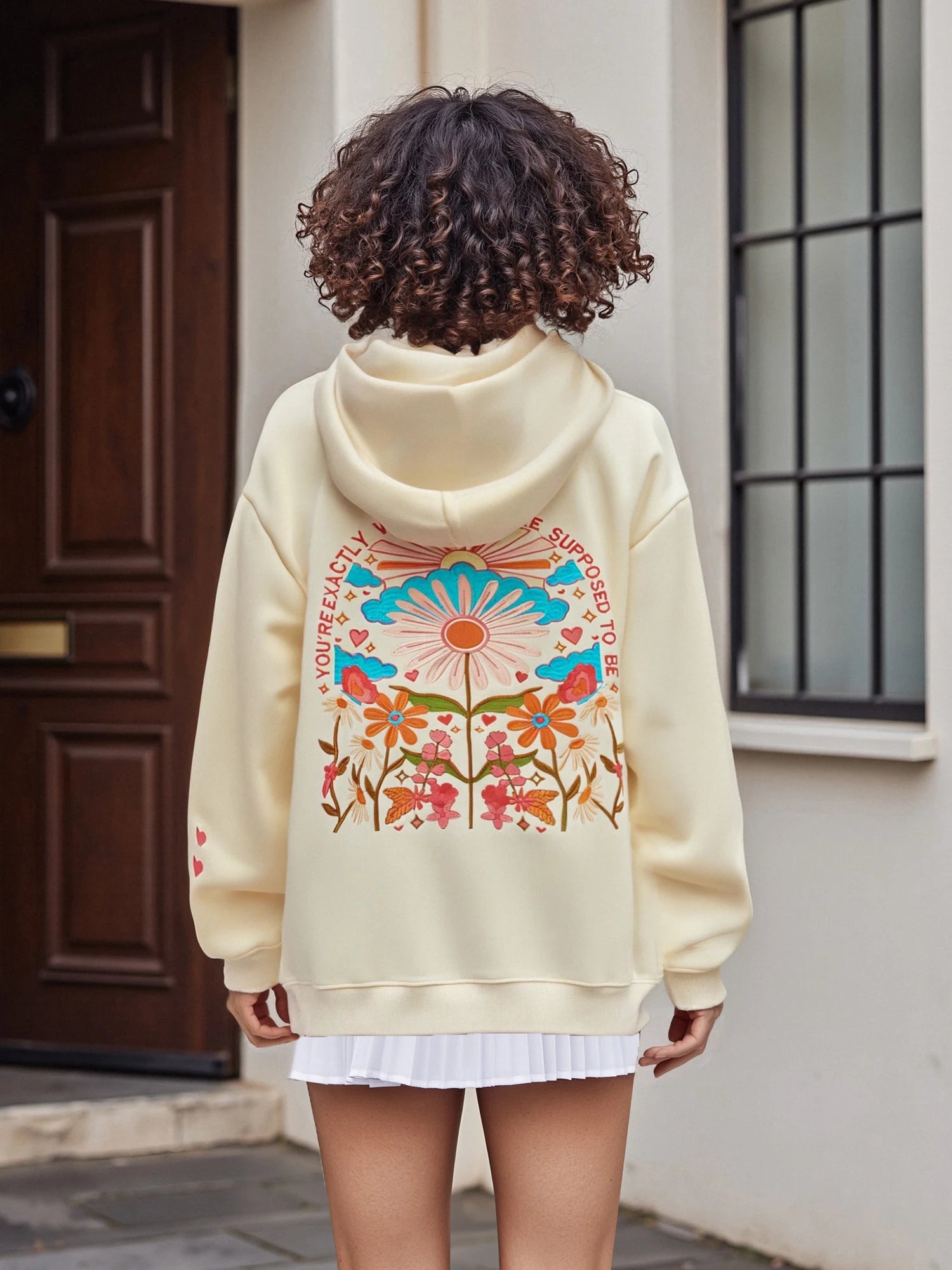 Person wearing a cream hoodie with colorful floral design outdoors.