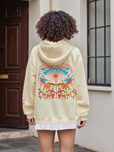 Person wearing a cream hoodie with colorful floral design outdoors.