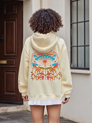 Person wearing a cream hoodie with colorful floral design outdoors.