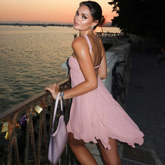 Woman in a pink dress standing by a waterfront at sunset