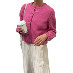 Person wearing a pink knitted cardigan holding a coffee cup