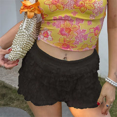 Person wearing a floral top and black ruffled shorts holding a pearl-handled bag.