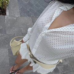 Person wearing a white polka dot dress with a beige handbag on a gray pavement.