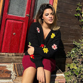 Woman sitting on a step wearing a black cardigan with colorful flower patterns in front of a red door.