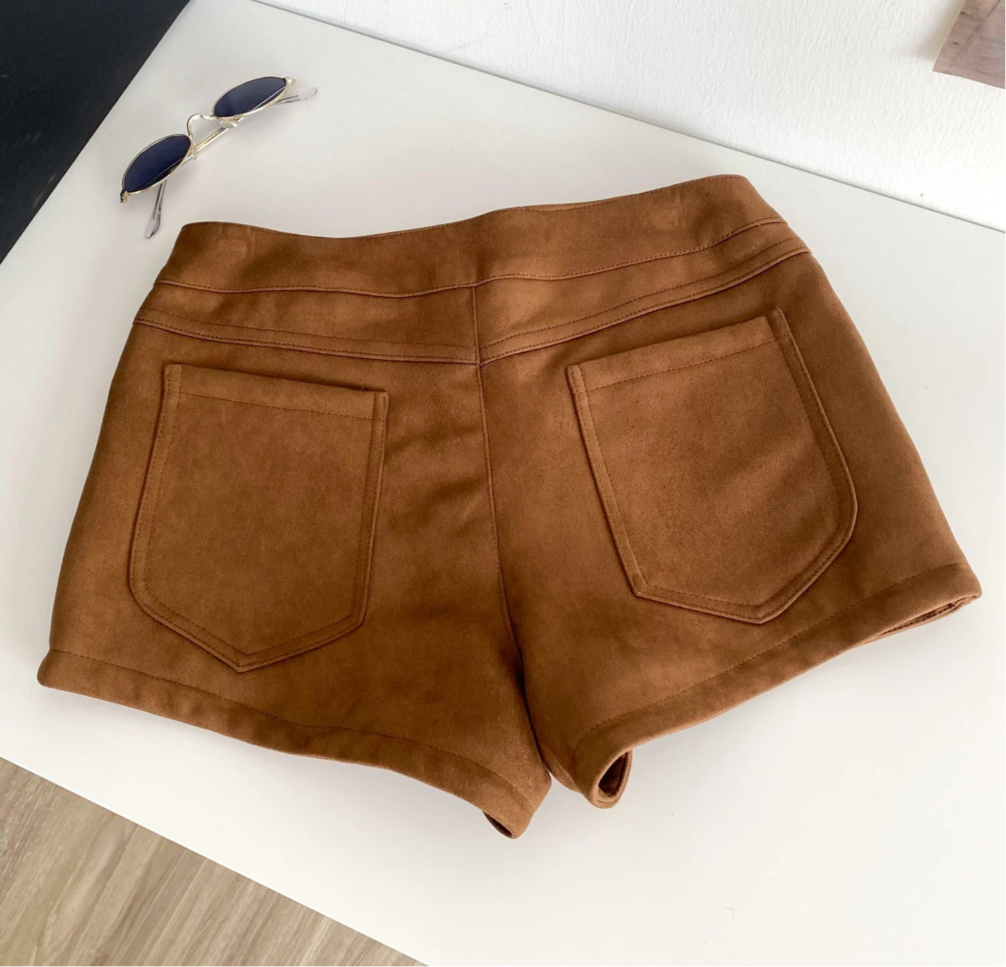 Brown shorts on a white surface with sunglasses - back view