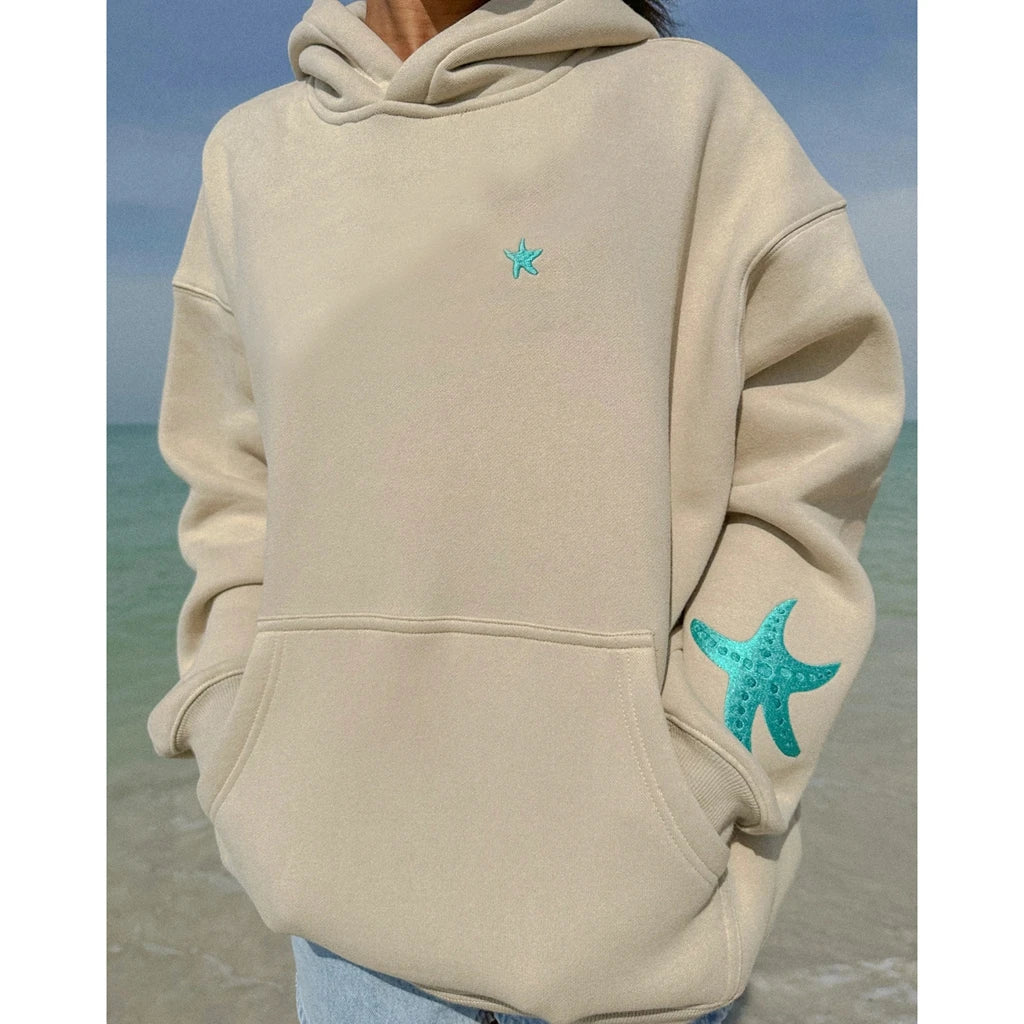 Beige hoodie with teal starfish designs on a beach