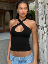 Woman wearing a black halter top and blue jeans standing against a rustic wall.