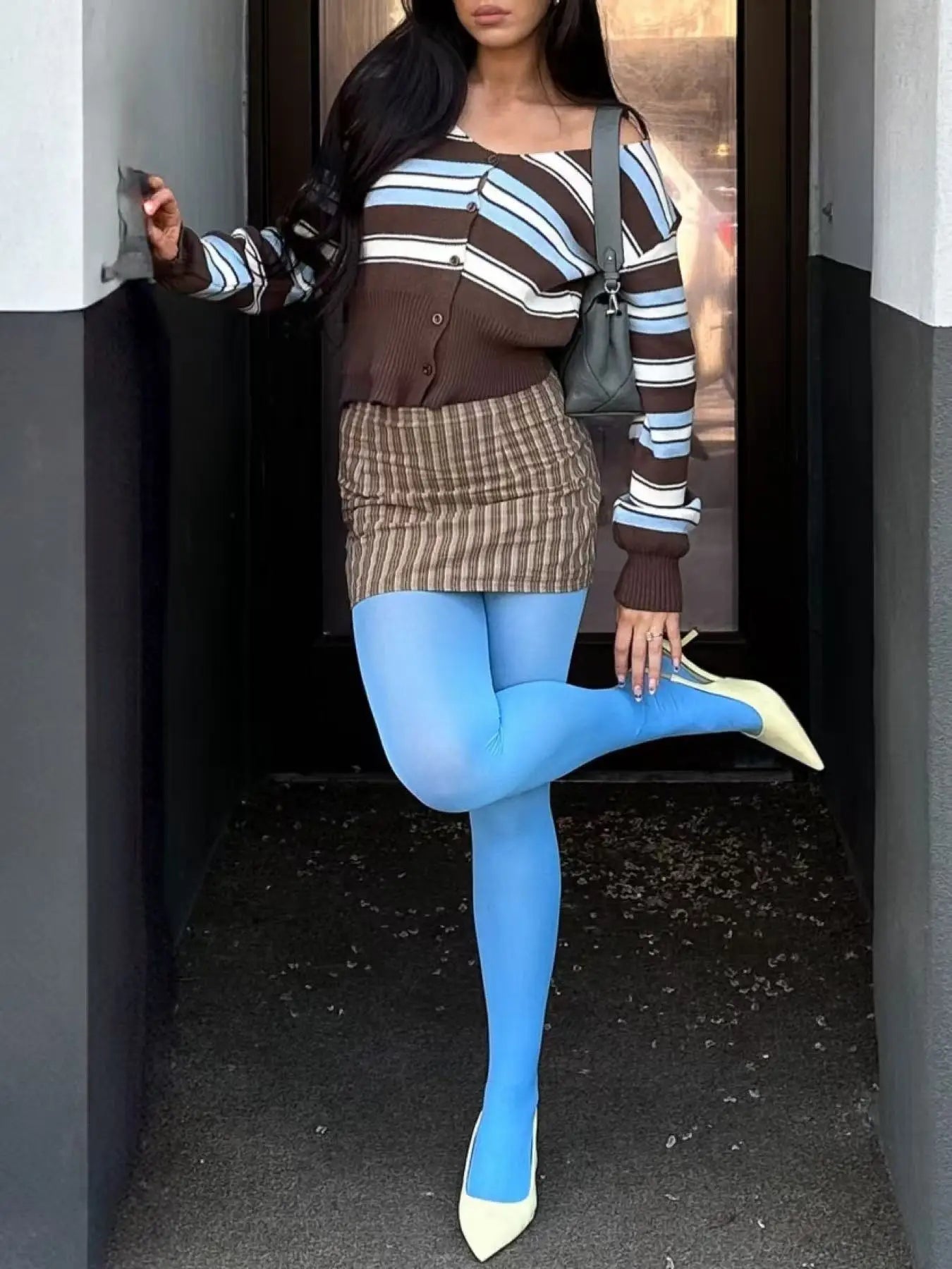 Person wearing a striped sweater, plaid skirt, and blue tights standing in a doorway.