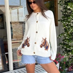 Woman wearing a white cardigan with horse designs outdoors.