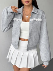 Woman wearing a gray jacket with lace details over a white top and skirt on a gray background