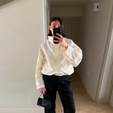 Person wearing a white blouse and black pants taking a mirror selfie.