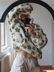 Person wearing a white sweater with green floral patterns, taking a mirror selfie.