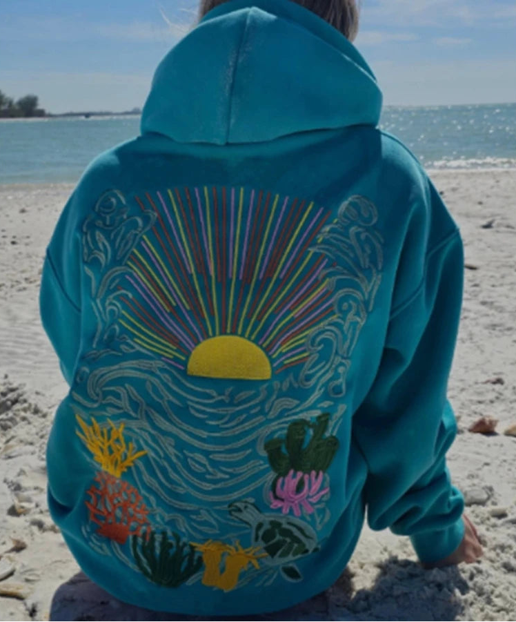 Person wearing a blue hoodie with ocean-themed design on a beach