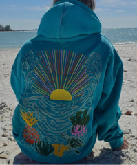 Person wearing a blue hoodie with ocean-themed design on a beach