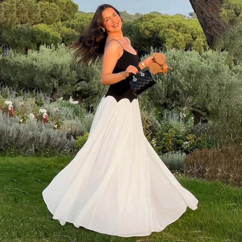 Woman in a black top and white skirt standing in a garden with greenery and flowers.