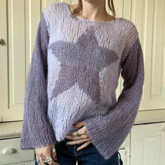 Person wearing a light purple sweater with star pattern in front of a white cabinet.