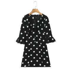 Black dress with white polka dots on a wooden hanger against a white background
