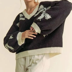 Person wearing a dark sweater with light-colored patterns on a neutral background