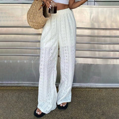 Person wearing white lace pants with a straw bag and drink in an urban setting