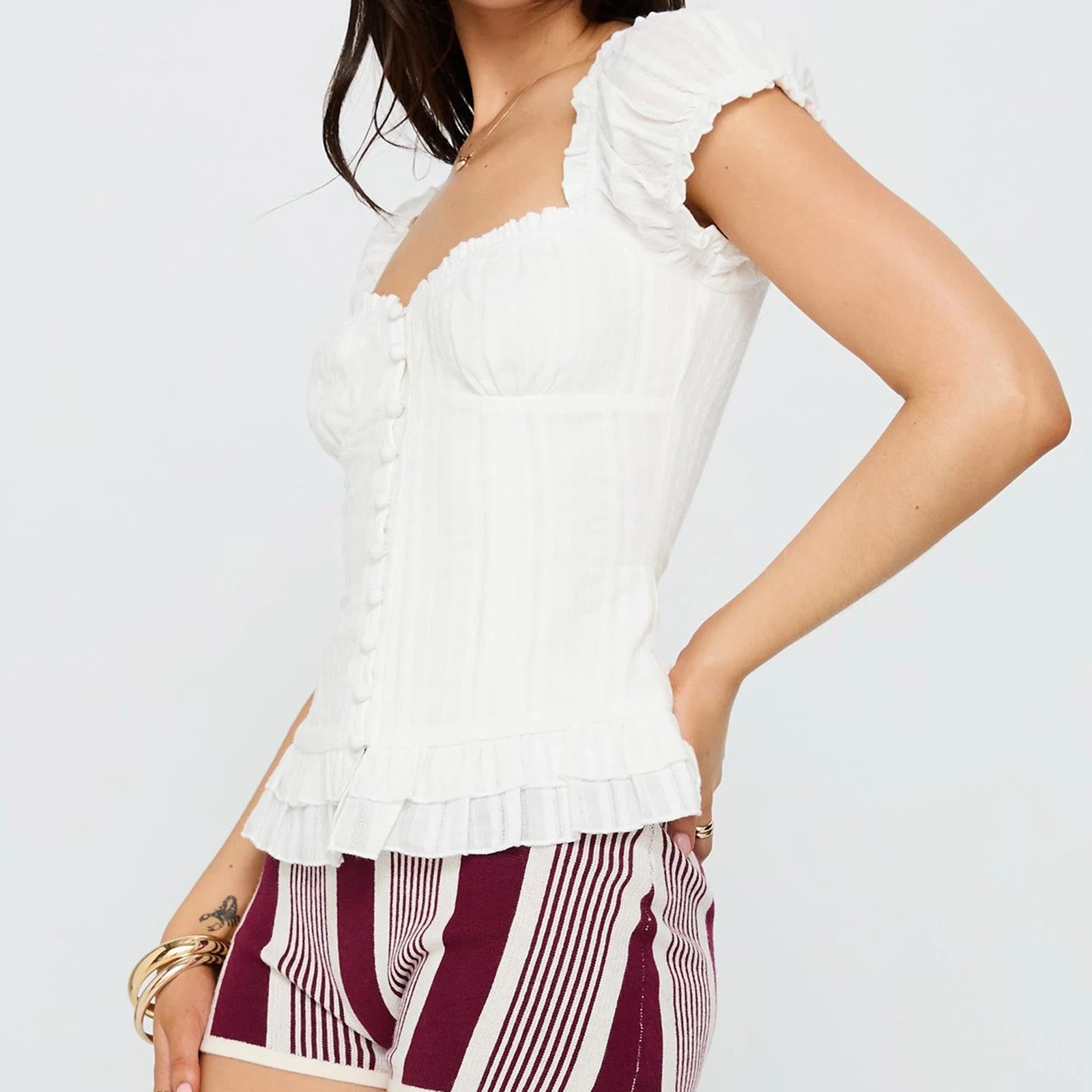 Woman wearing a white ruffled top and patterned shorts on a light gray background