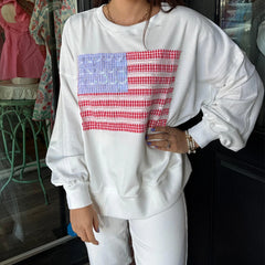 Person wearing a white sweatshirt with a colorful checkered design in a casual setting.