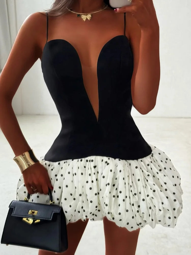 Person wearing a black top and white polka dot skirt holding a black handbag.