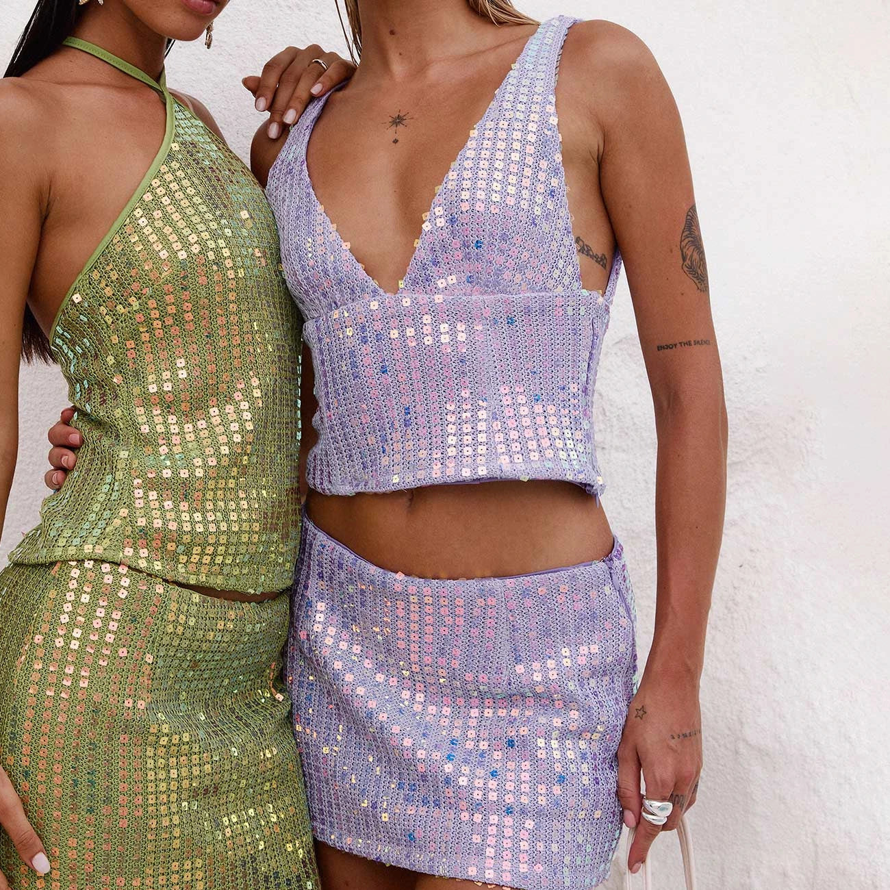 Two women wearing sparkly outfits against a white background