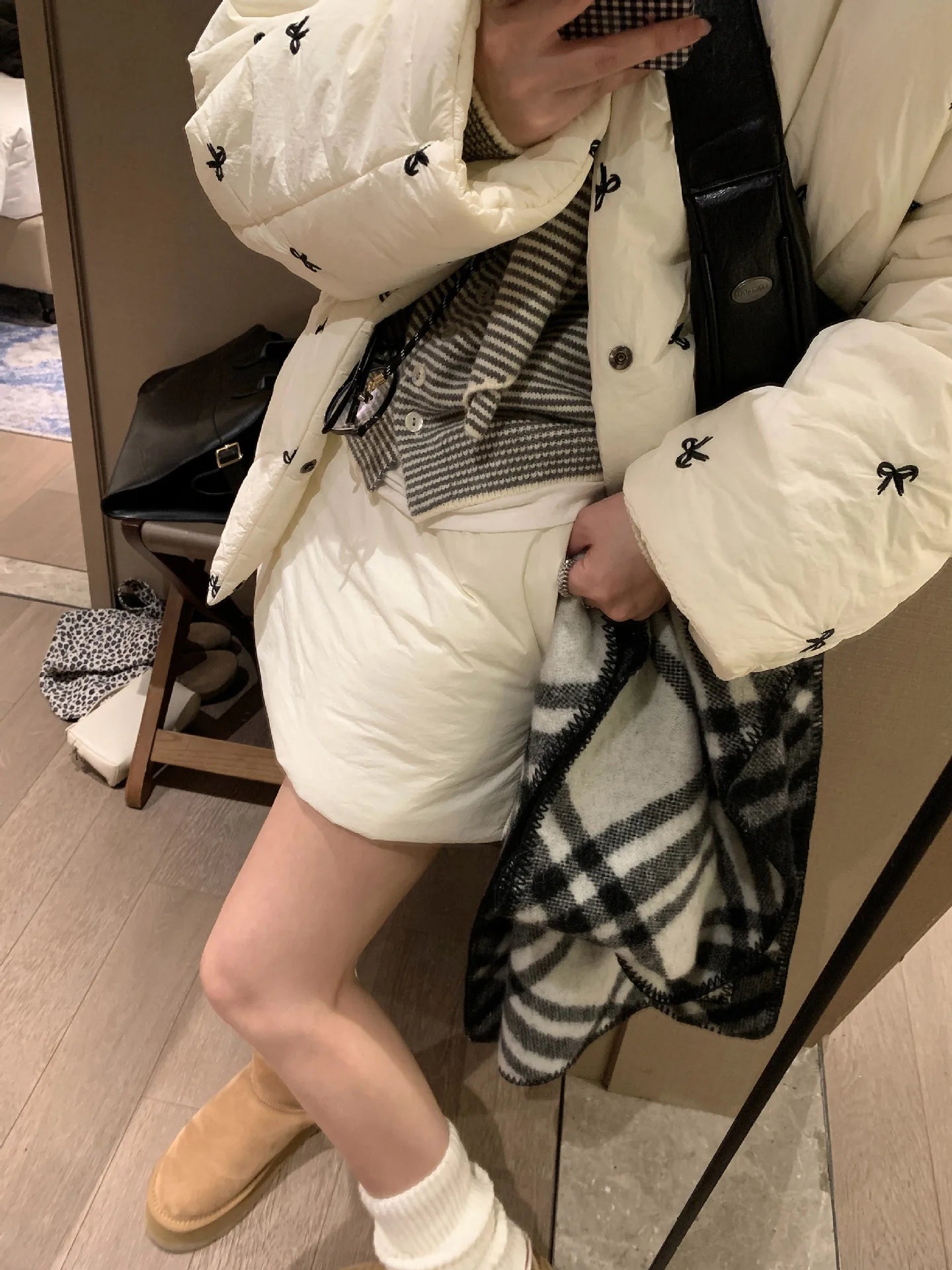 Person wearing a white puffer jacket with black accents, white shorts, and tan boots in an indoor setting.
