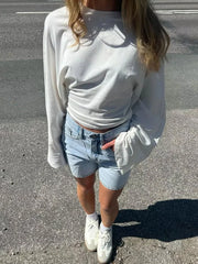Person wearing a white sweatshirt, light blue denim shorts, and white sneakers on a street.