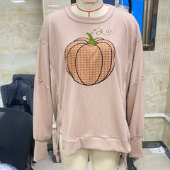 Pink sweatshirt with a pumpkin design on a mannequin against a tiled wall.
