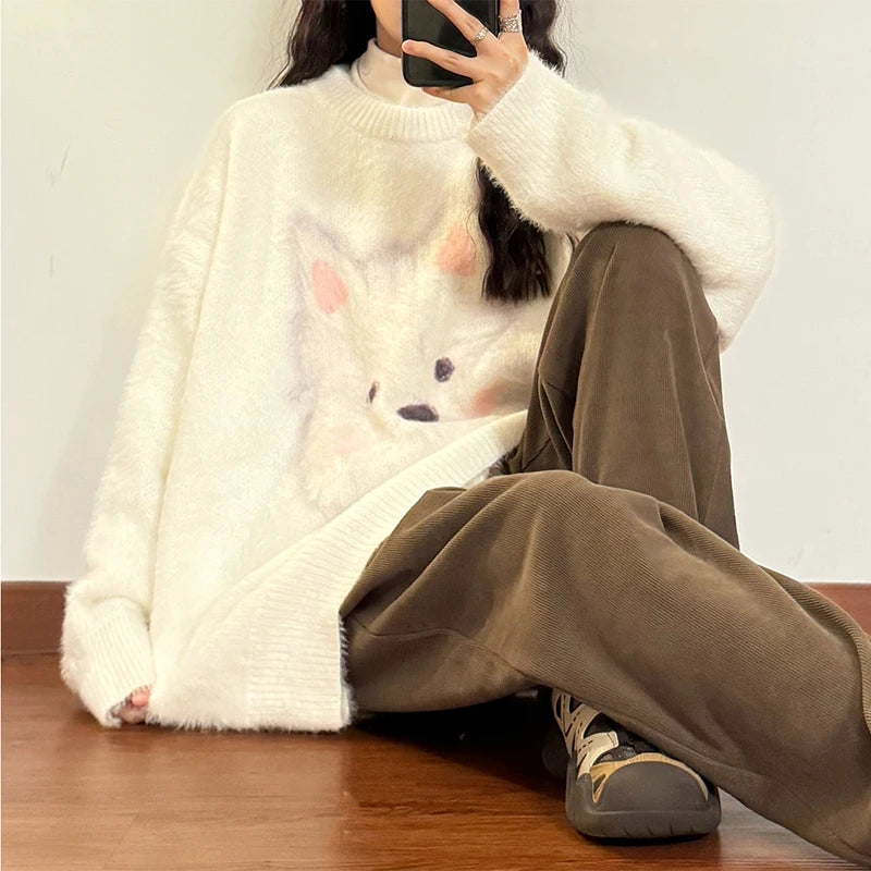 Person wearing a white sweater with a cartoon design and brown pants sitting on a wooden floor.