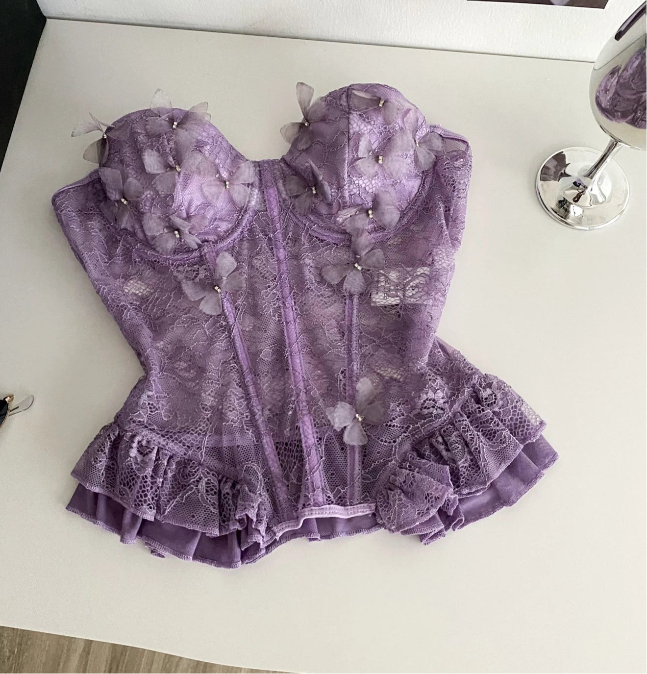 Purple lace dress on a white surface with sunglasses and a glass of wine in the background.