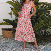 Woman wearing a pink floral dress standing in front of green plants.