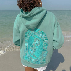 Person wearing a teal hoodie with a design on the beach