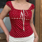 Red polka dot top with white skirt worn by a person, indoors.
