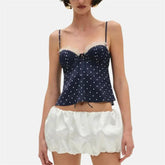 Woman wearing a navy blue polka dot corset top and white satin shorts