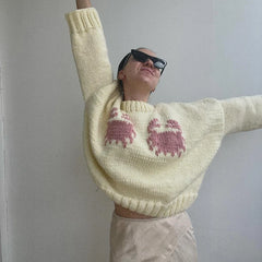 Person wearing a light yellow sweater with pink cat patterns against a plain background