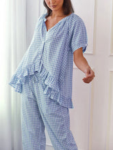 Woman wearing a blue checkered pajama set in a room with white walls.